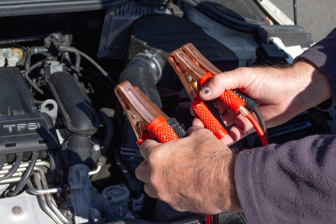 gallery-2 Close-up of hands holding jumper cables near a car engine, ready for repair.