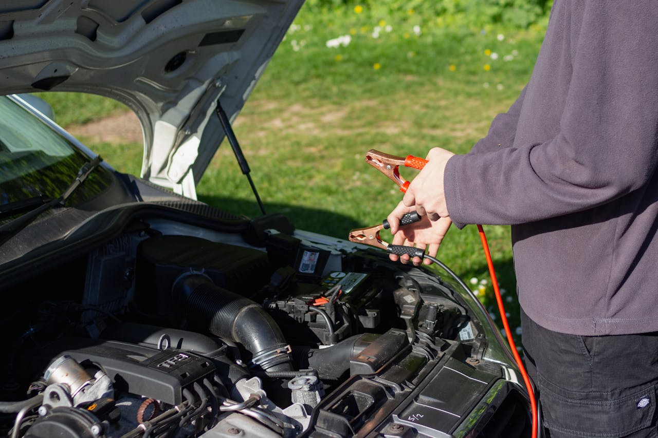 gallery-1 Man using jumper cables on car engine outdoors on a sunny day. Vehicle maintenance and repair concept.